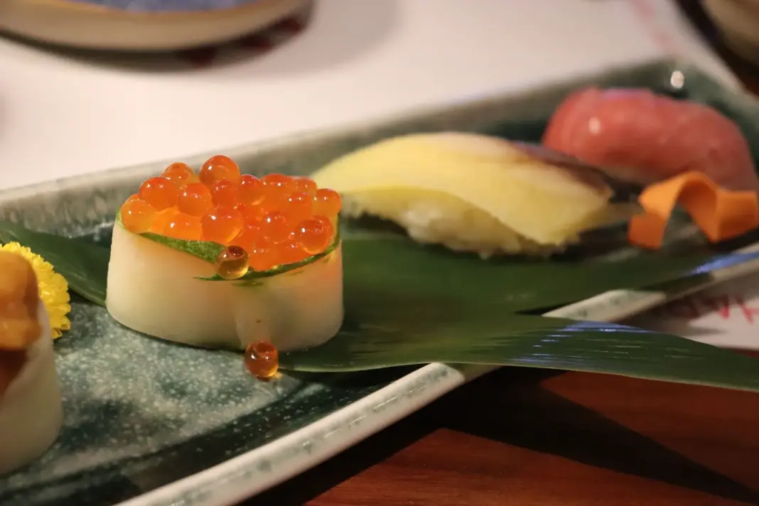Primer plano de un plato de sushi que presenta ikura, sashimi y nigiri en un plato decorativo.